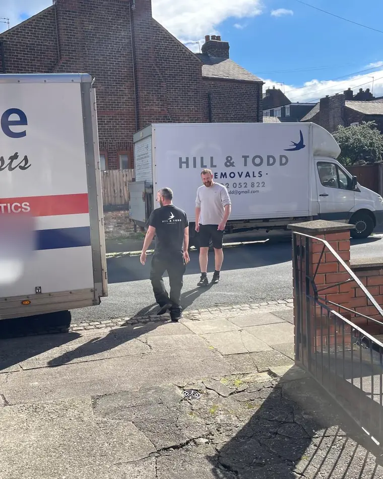 The white Hill and Todd Removals Luton van with the swallow logo, two of the team walking towards it