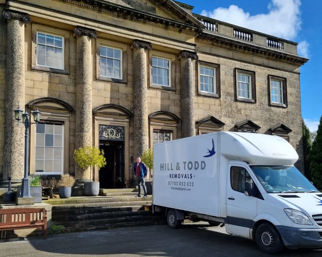 Hill and Todd Removals van on a job, parked outside a large stone country house with columns, one of the team at the front door
